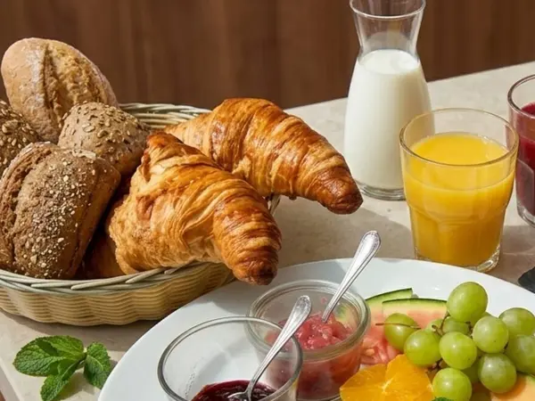 Brotkorb mit frischen Brötchen und Croissants, Konfitüre und einem Glas Orangensaft