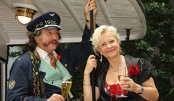 Schaffner in historischer Uniform stößt beim Familienbrunch mit einem Gast mit einem Glas Sekt an