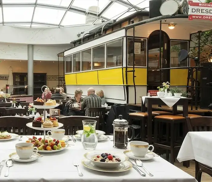 Gedeckter Frühstückstisch mit Etagere im Innenraum, dahinter die gelbe historische Straßenbahn Helene unter der Glaskuppel
